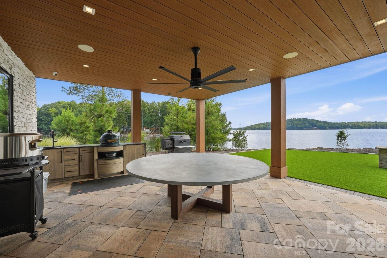 Covered lower-level patio and summer kitchen at 123 Cove Point with a large round table and lake views